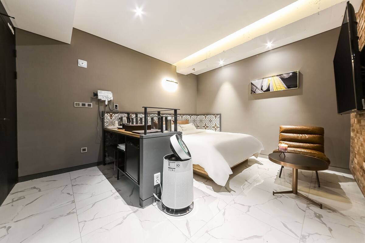 Habitación de hotel pequeña con cama, escritorio con silla, una mesita y televisor montado en la pared.