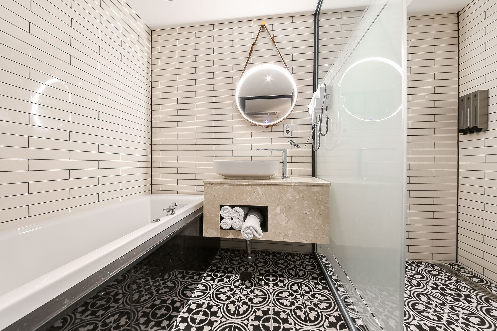 A bathroom with a white bathtub, a sink with a mirror, and patterned black and white tiles.