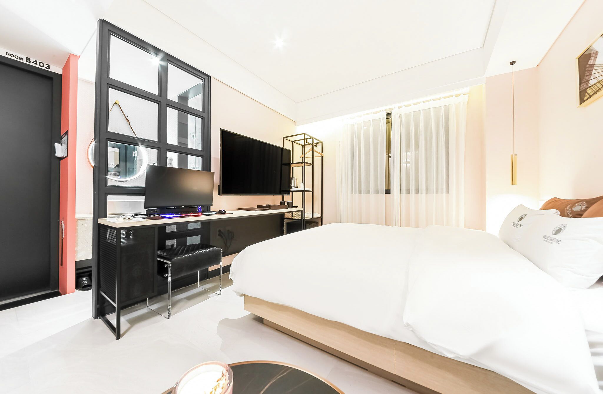 A modern hotel room with a large bed, a desk with a computer and TV, a chair, and a wardrobe.
