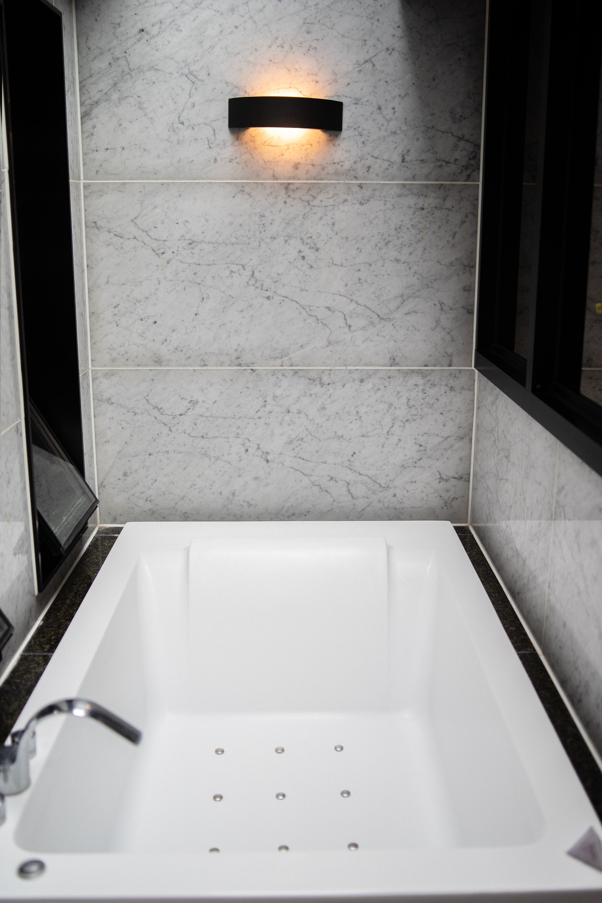 A modern bathroom with a white bathtub, a wall-mounted light fixture, and a marble backsplash.