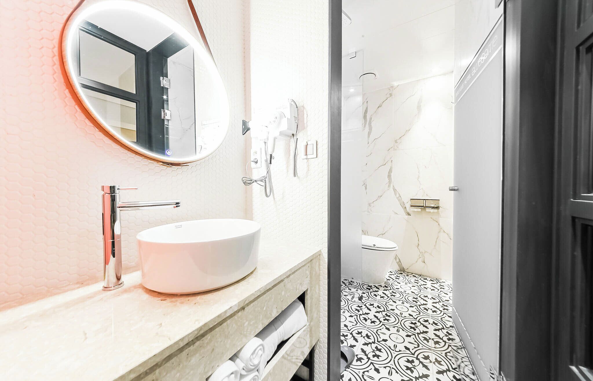 A modern bathroom with a round mirror, a white sink, and a shower area.