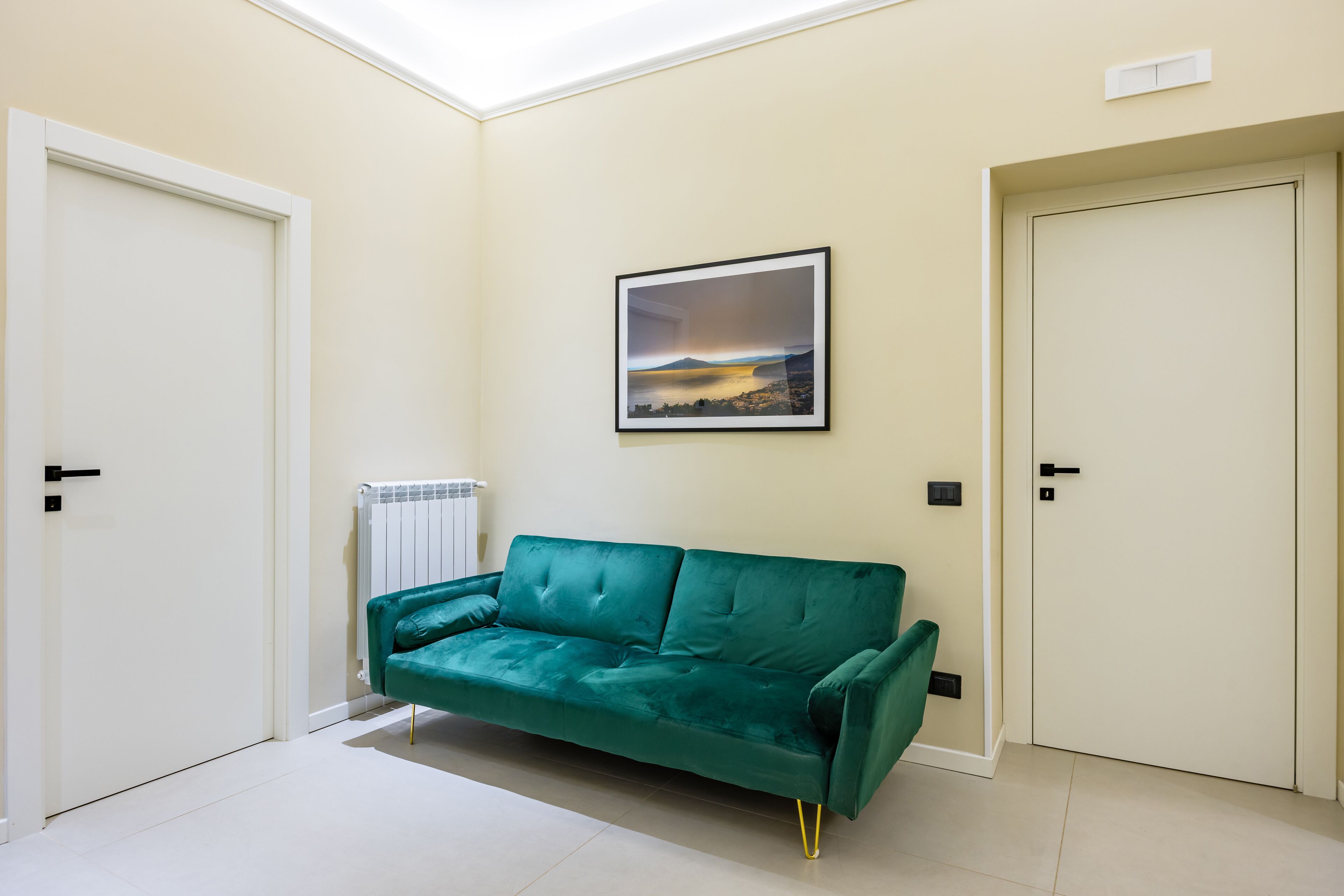 A room with a teal sofa, two white doors, and a framed picture on the wall.