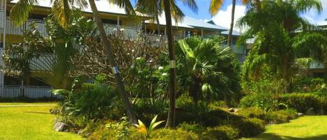 A hotel with a lush garden, palm trees, and a building with balconies.
