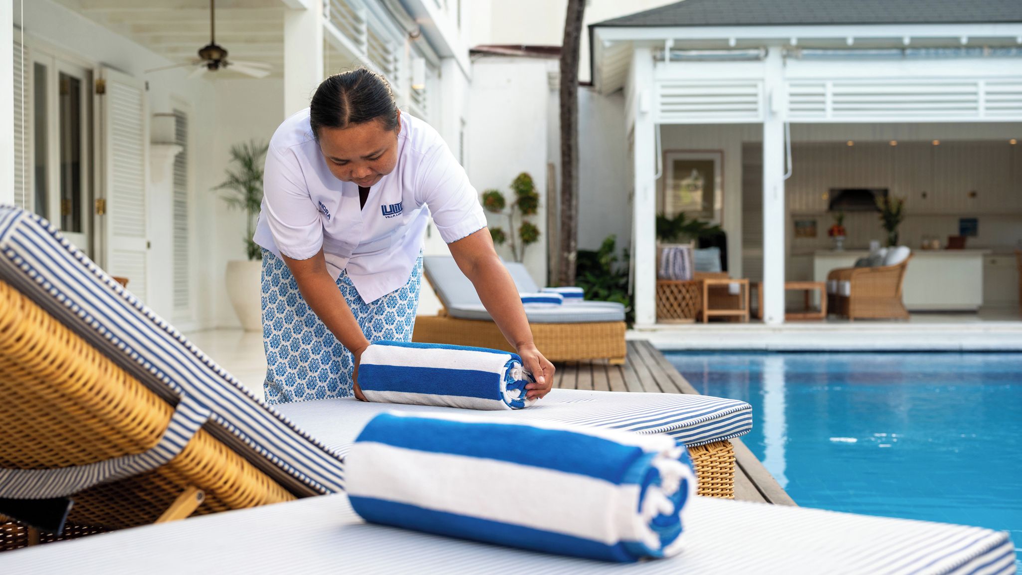 A poolside area with lounge chairs, a pool, and a person adjusting a towel.