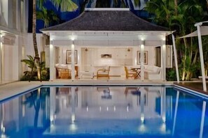A poolside area with a covered seating area, lounge chairs, and a dining table.