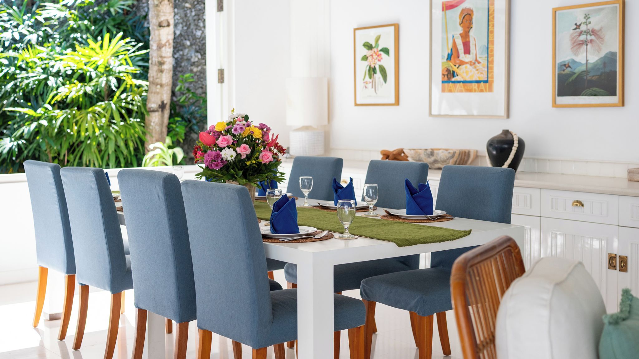 A dining area with a white table, blue chairs, and a floral centerpiece.