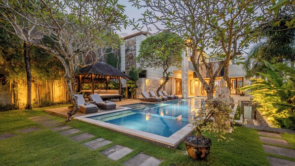 A swimming pool with lounge chairs, a gazebo, and a Buddha statue.