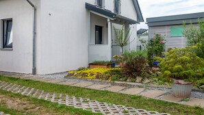 Ein modernes Gebäude mit weißer Fassade, ein kleiner Garten mit gelben Blüten und ein Topfpflanzen.