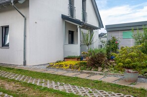 A modern building with a white facade, a small garden with yellow flowers, and a potted plant. - Apartment 'Im Fränkischen Seenland' with Private Terrace and Wi-Fi (Abenberg)