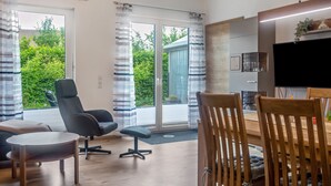 Ein modernes Wohnzimmer mit einer Couch, Sesseln, einem Esstisch und einem Fernseher.