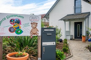 Ein Gebäudeeingang mit Schild, Briefkasten und Garten.