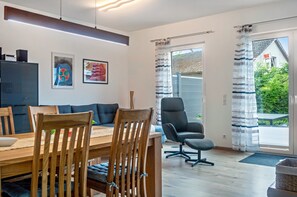 A modern living room with a dining area, a black office chair, and a large window with curtains. - Apartment 'Im Fränkischen Seenland' with Private Terrace and Wi-Fi (Abenberg)