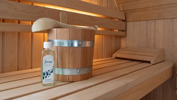 Een sauna met een houten bank, een houten emmer en een fles Fichtner Saunadust.