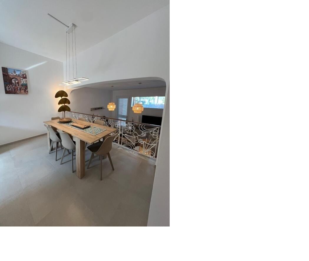 Zona pranzo moderna con tavolo e sedie in legno, illuminazione a sospensione e vista sull'esterno.