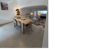 A modern dining area with a wooden table and chairs, pendant lighting, and a view of the outdoors.
