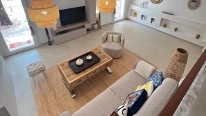 A modern living room with a sofa, coffee table, and a TV. There are two hanging lamps and a fireplace.