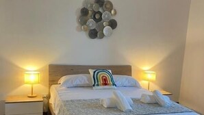A neatly arranged bedroom with a bed, bedside tables, a decorative wall piece, and a black ottoman.