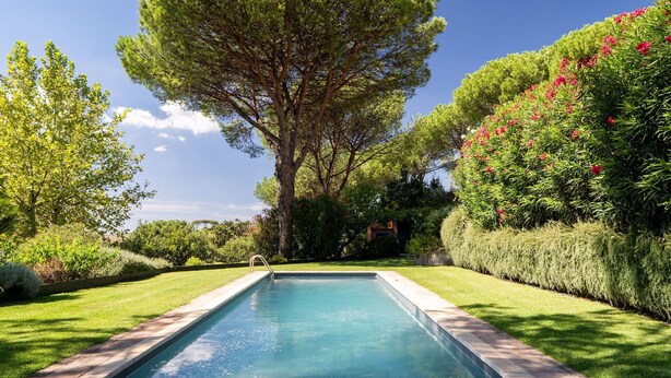 A swimming pool with a clear blue water surface, surrounded by well-maintained grass and various trees and shrubs. - Luxury Villa Nearby South Rome (Falcognana Di Sopra)