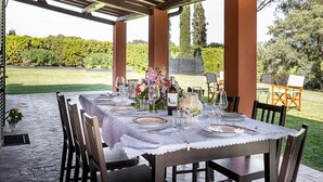 An outdoor dining area with a table set for six, covered with a white tablecloth, surrounded by wooden chairs. - Luxury Villa Nearby South Rome (Falcognana Di Sopra)