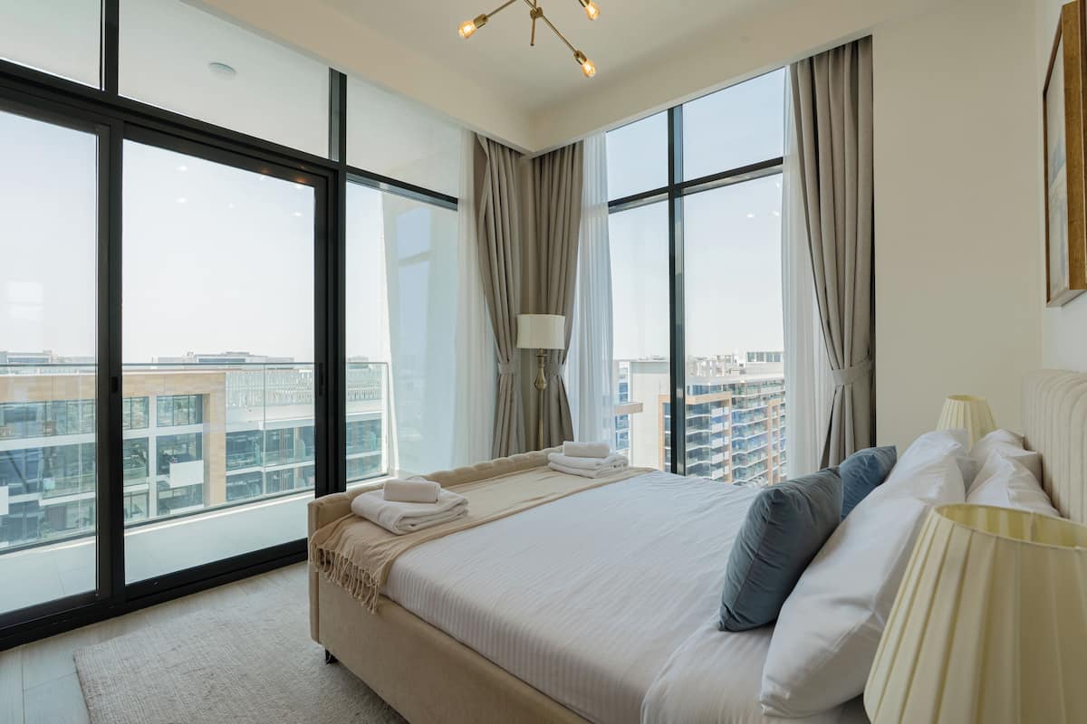 A modern hotel room with a large bed, a view of the city, and a cityscape visible through the windows.