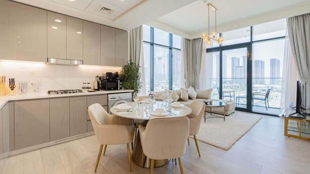 A modern kitchen with a dining area, large windows, and a city view. - Azizi Riviera Residences - Meydan (Dubai)