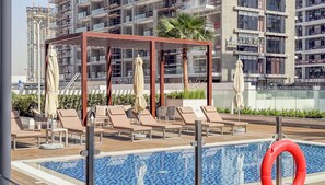 A rooftop pool area with lounge chairs, umbrellas, and a pool with a lifebuoy.