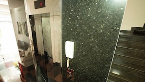A polished black marble wall with a telephone mounted on it, a glass elevator door, and a staircase to the right. - Ben Thanh Retreats Hotel (Ho Chi Minh City)