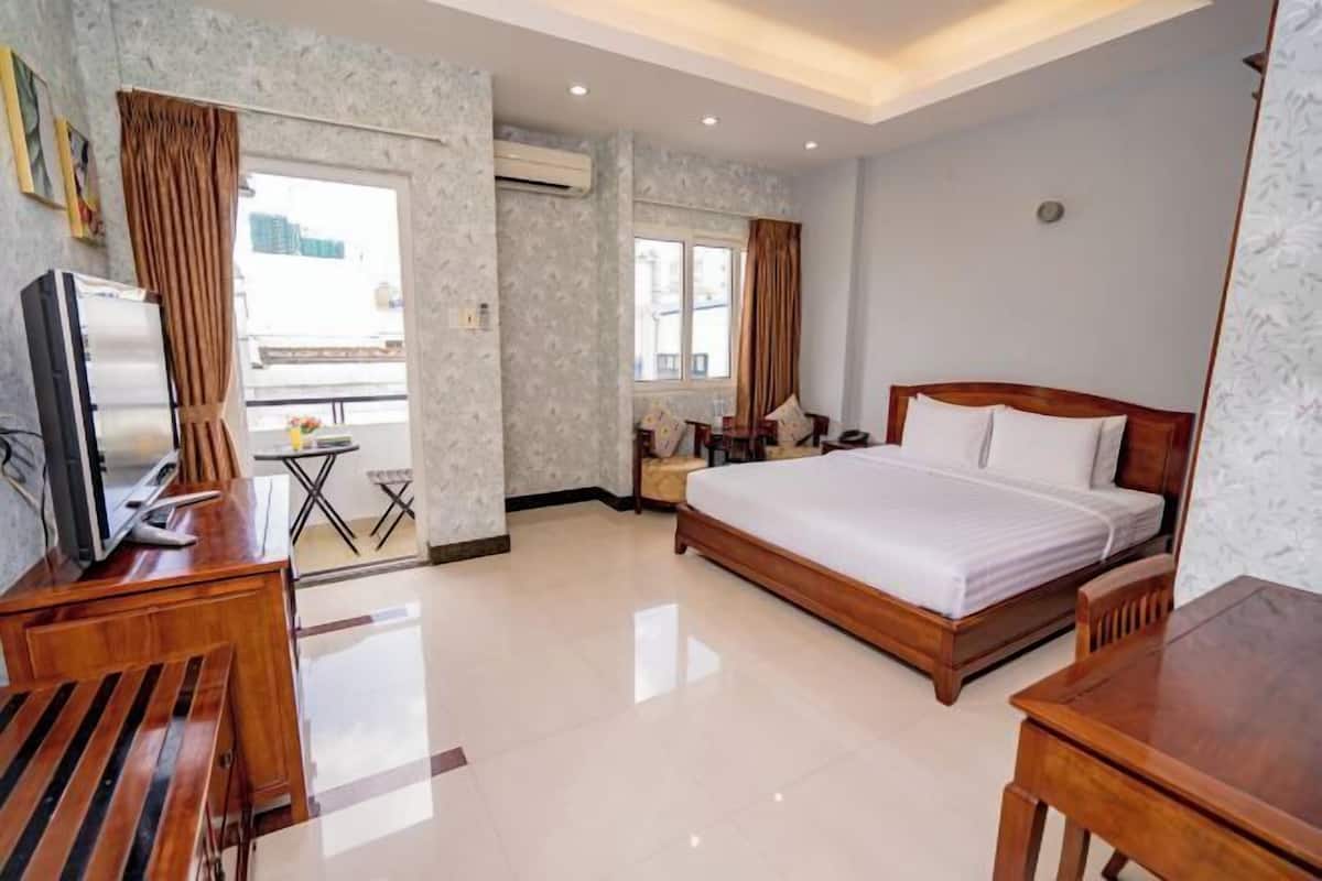 A hotel room with a bed, a desk, a chair, a TV, a small table, and a window.