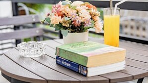 A table with a book titled 'Vietnam,' a glass of orange juice, and a flower arrangement. - Ben Thanh Retreats Hotel (Ho Chi Minh City)