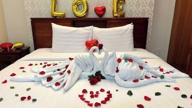 A bed with rose petals and swans made of towels, a red rose, and the word 'LOVE' in gold balloons. - Ben Thanh Retreats Hotel (Ho Chi Minh City)