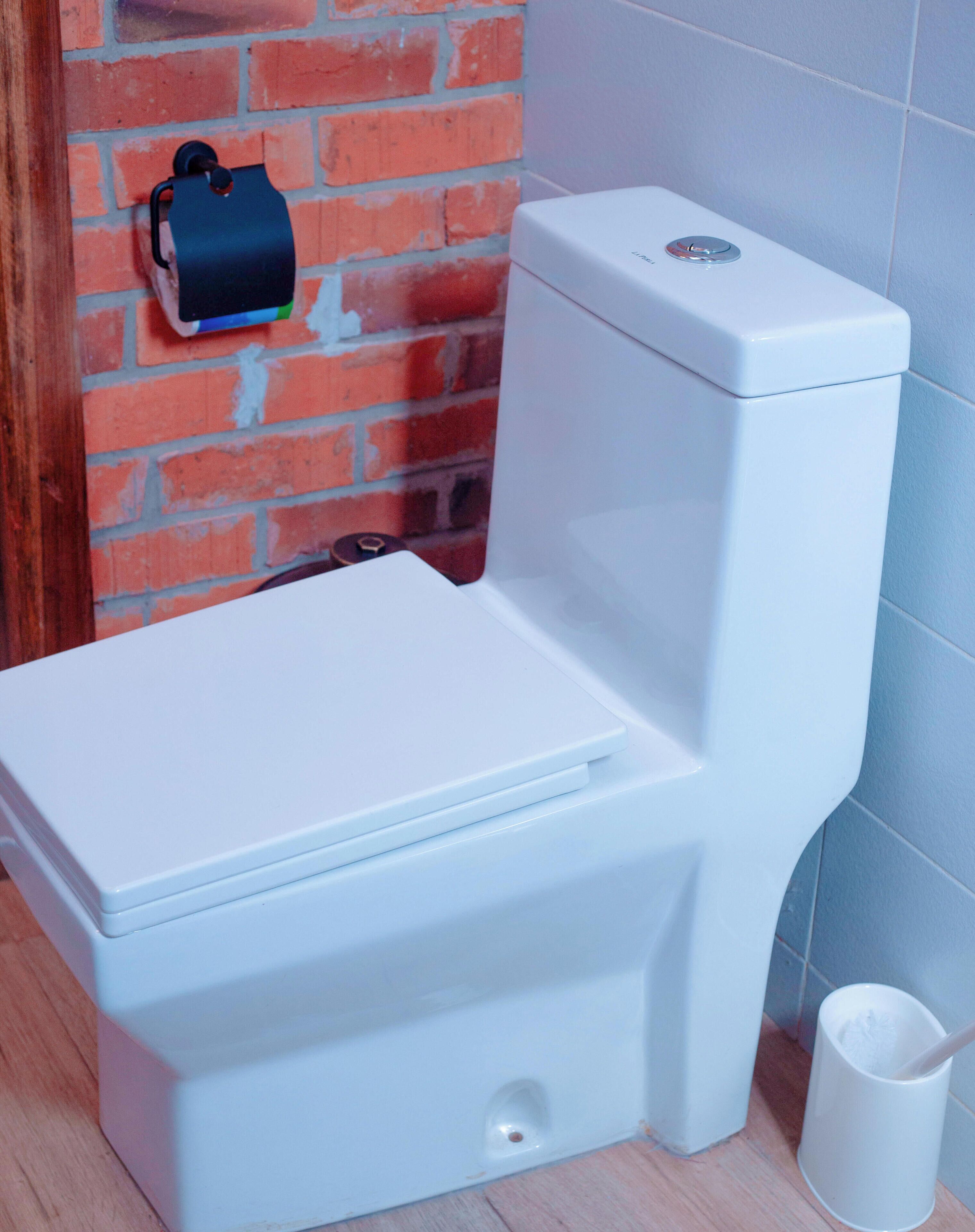 A white toilet in a bathroom with a brick wall and a blue-tiled wall.