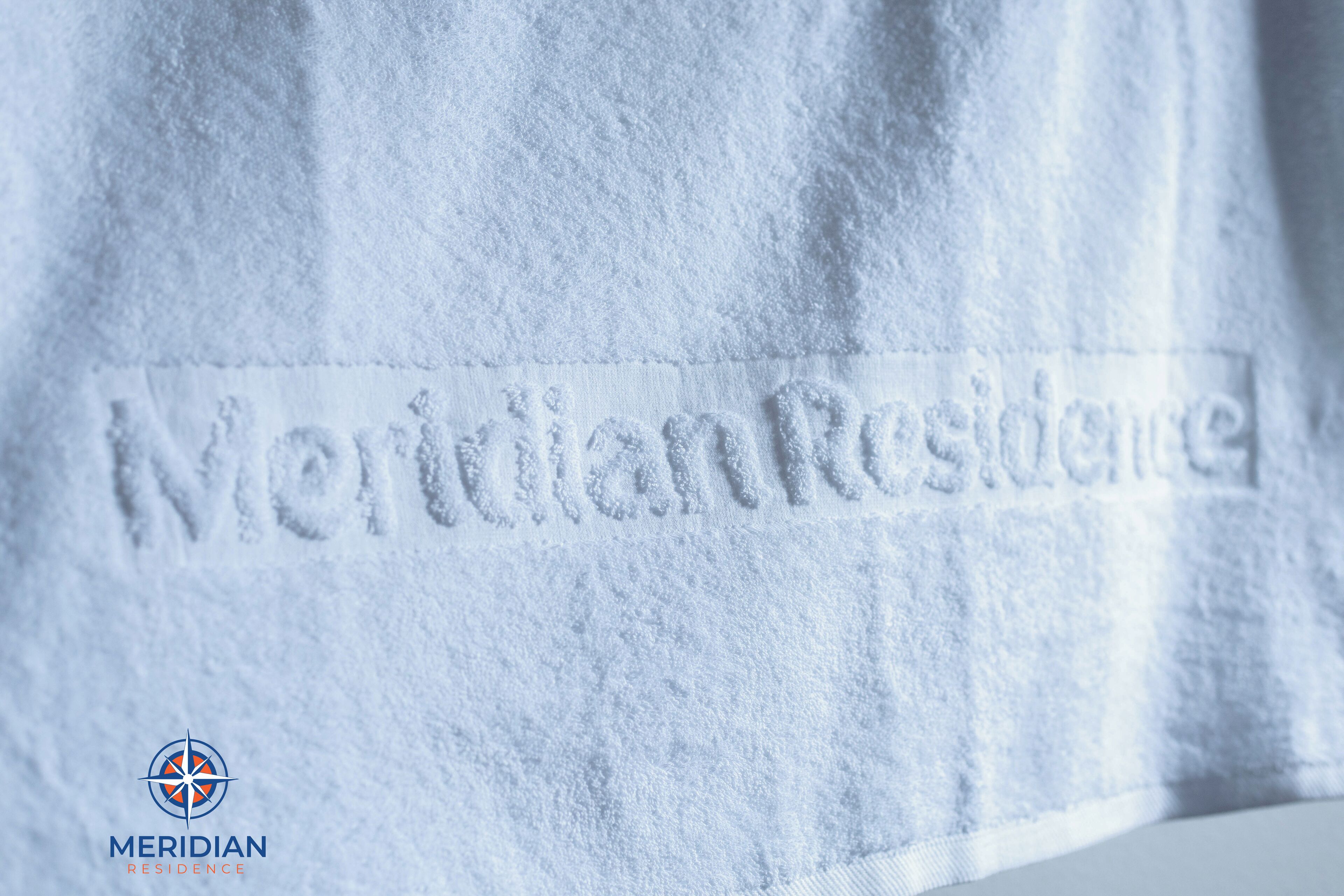 A close-up of a towel with the text 'Meridian Residence' embossed on it.