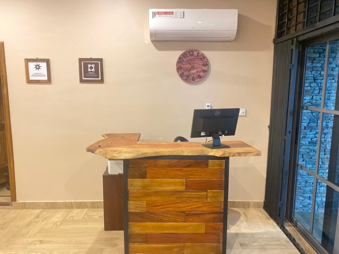 A reception desk with a wooden top and a monitor, an air conditioner, framed certificates on the wall, and a clock.