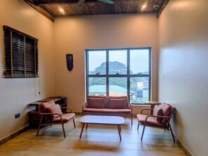 A room with a sofa, two armchairs, a coffee table, a window with a view, and a ceiling fan. - Meridian Residence (Tema)