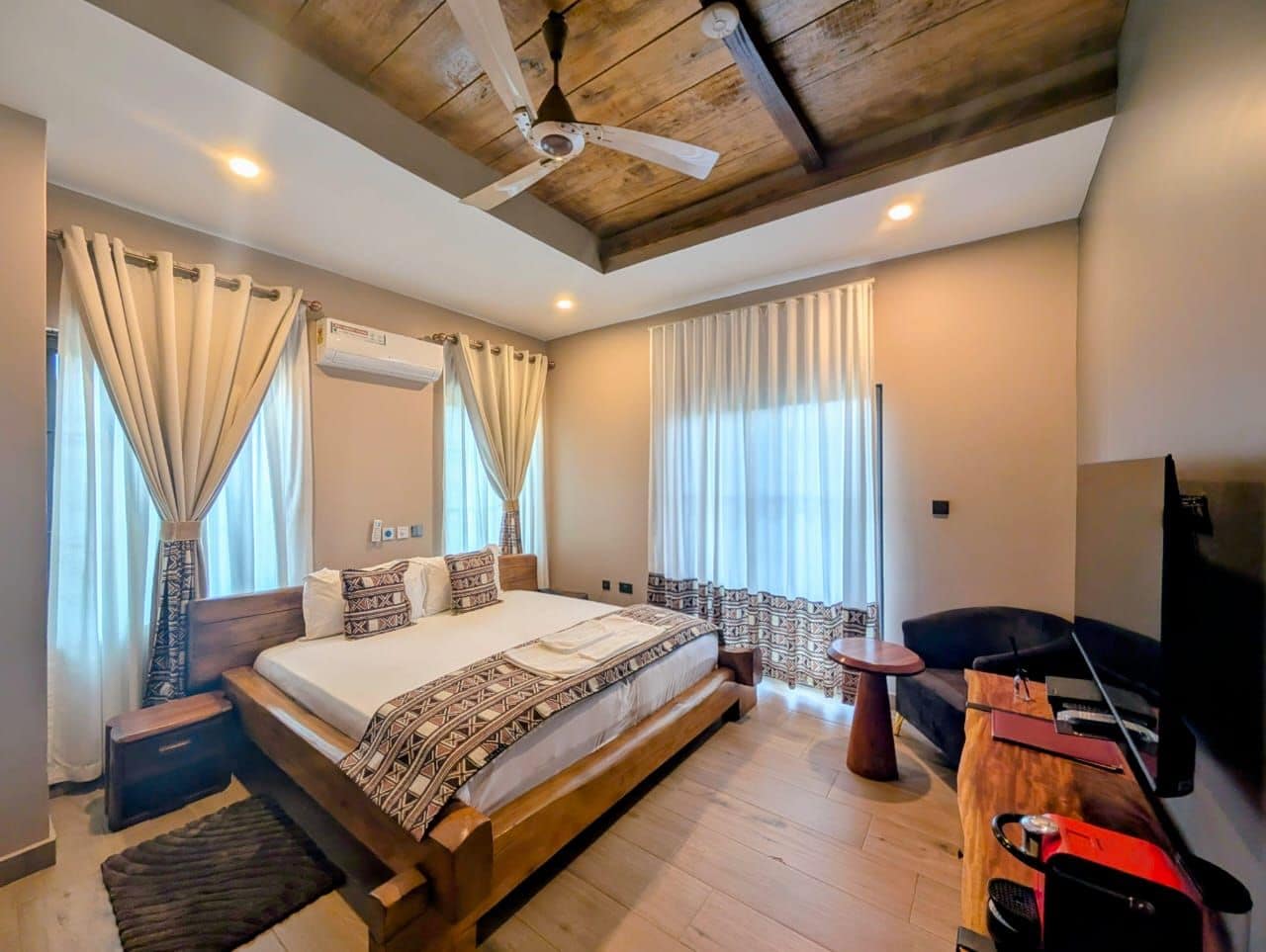 A bedroom with a large bed, a ceiling fan, a TV, and a seating area with a table and chairs.