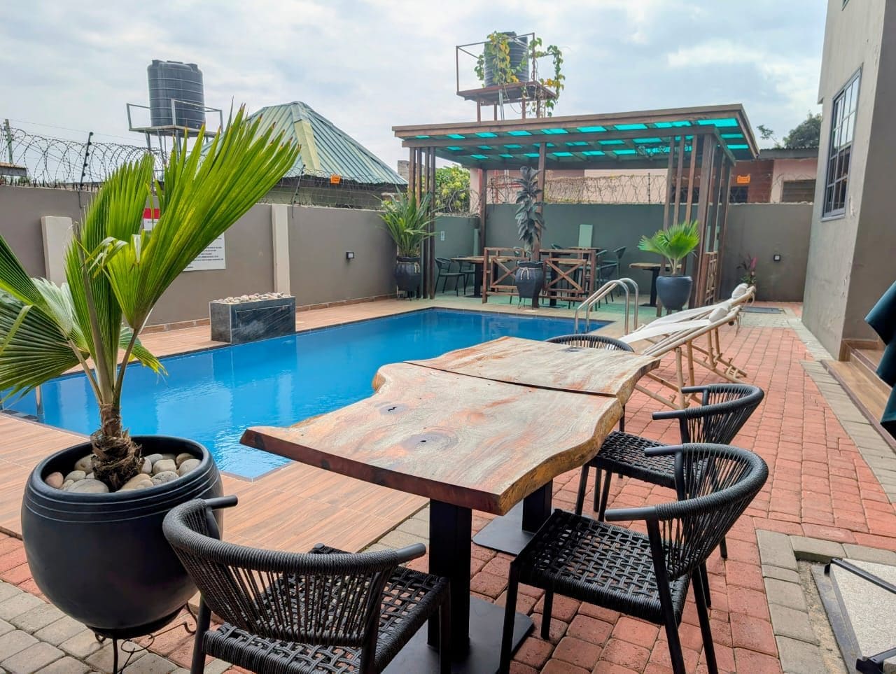 Un área de piscina en la azotea con una mesa y sillas de madera, rodeada de plantas en macetas.