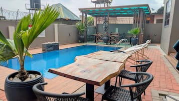 Un área de piscina en la azotea con una mesa y sillas de madera, rodeada de plantas en macetas.