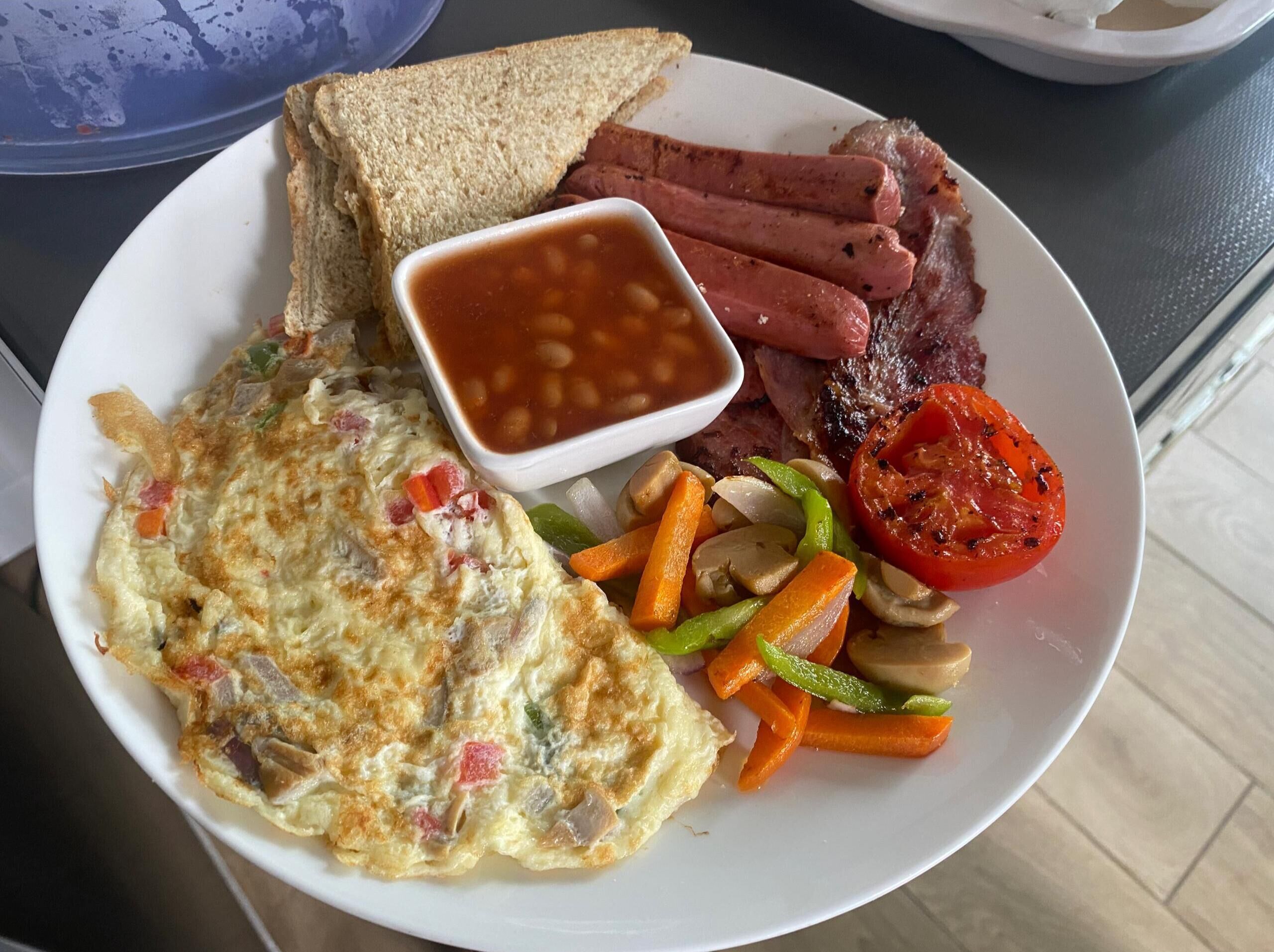 Een bord met toast, worstjes, steak, bonen, een omelet en groenten.