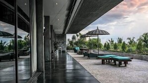 A modern outdoor lounge area with a wet floor, glass walls, and outdoor seating. - Villa Mana | 7BR Tropical Estate Near Canggu Beach w/ Chef (Badung)