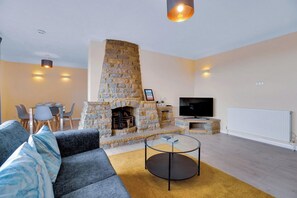 A living room with a stone fireplace, a television, a sofa, and a dining area with chairs.