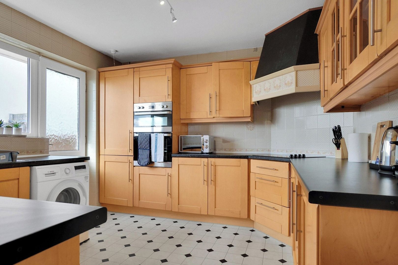 A kitchen with wooden cabinets, a built-in oven, a microwave, and a washing machine.