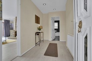 En hall med en vit dörr, en brun matta, ett litet bord med en växt och en eldstad i sten.