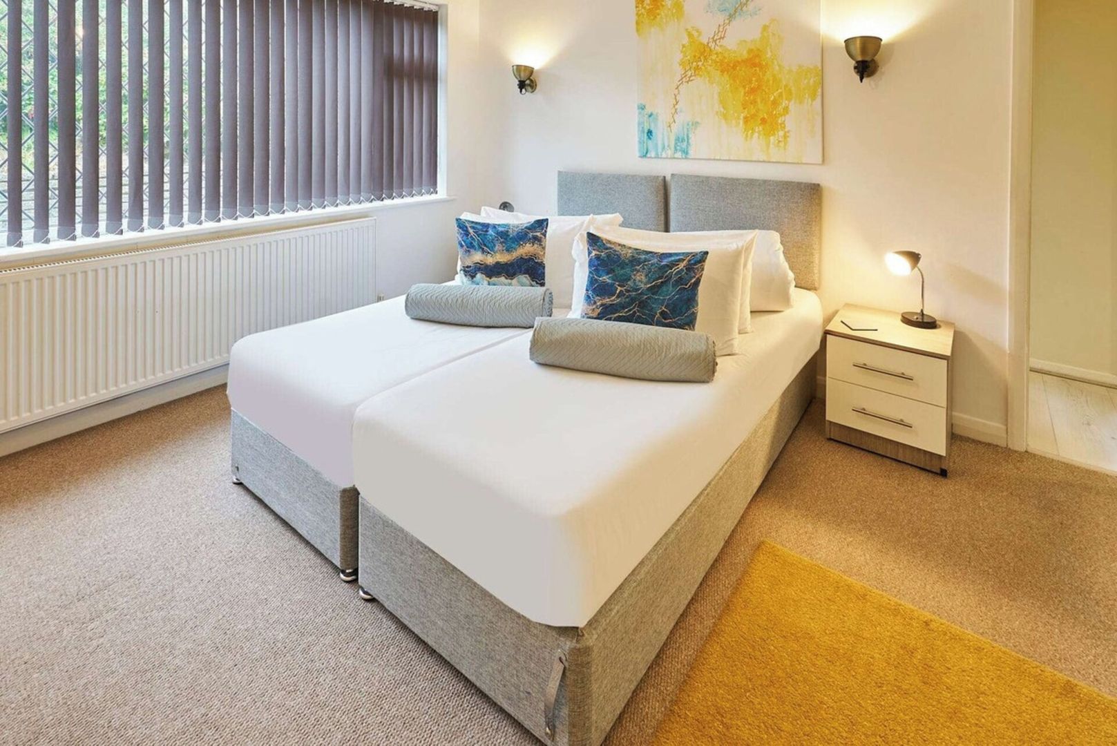 A modern bedroom with a bed, bedside tables, and a window with blinds.