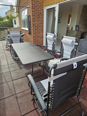An outdoor patio area with a metal table and chairs, a brick wall, and a glass door leading to an interior space.
