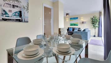 A dining area with a glass table set for six, a sofa, a TV, and a painting of a van.