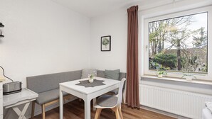 A compact living space with a dining table, a bench, and a window with a view of greenery.
