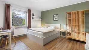 A bedroom with a bed, a desk, a chair, a window, and a wardrobe.