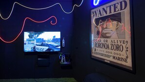 A room with a mounted TV displaying a police car, a poster with a wanted poster, and a neon light.