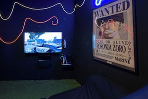 A room with a mounted TV displaying a police car, a poster with a wanted poster, and a neon light.