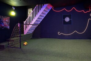 A room with a soccer goal, a staircase, and a wall with neon lights.